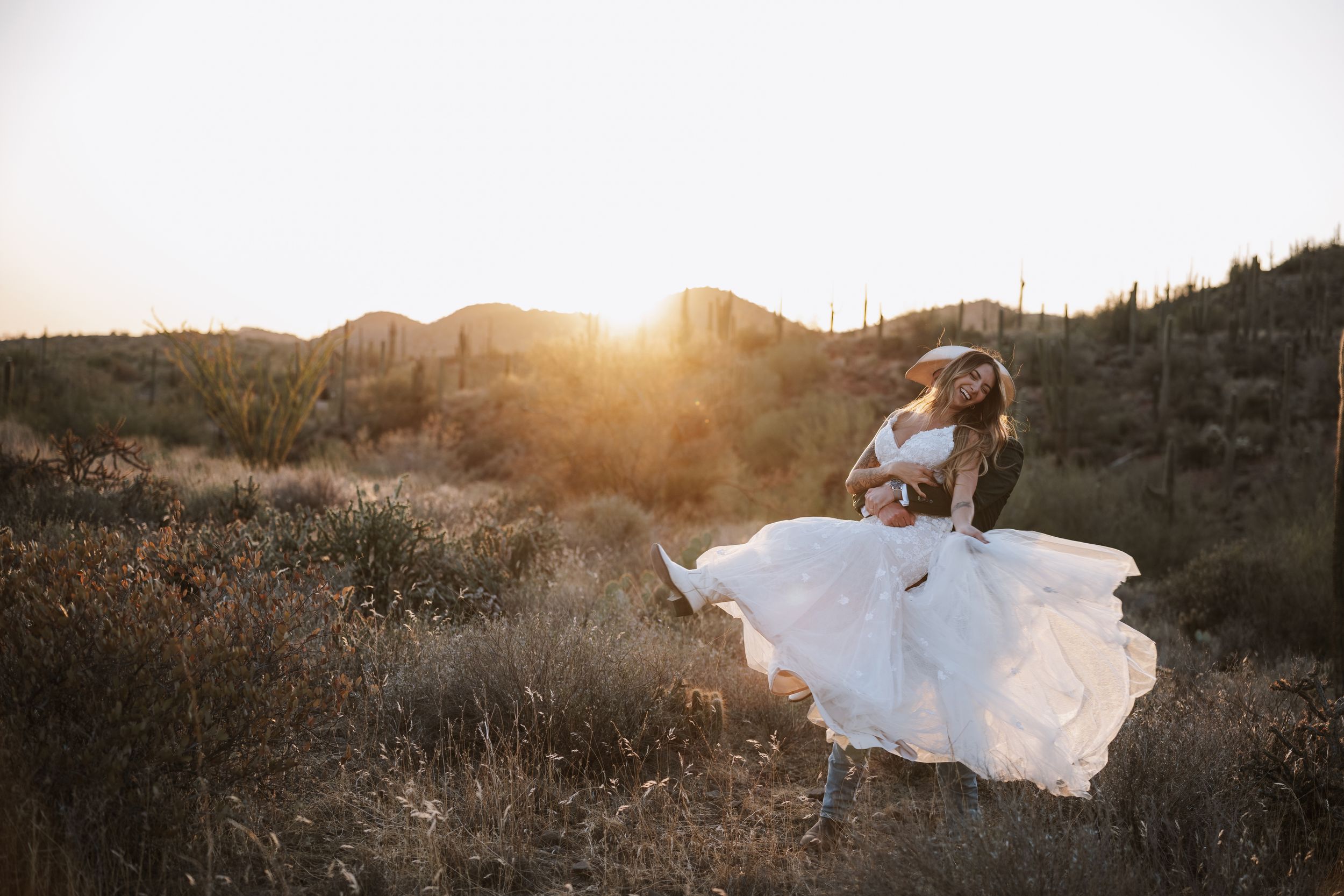 Groom playfully picking up bride and swinging her around in the desert.