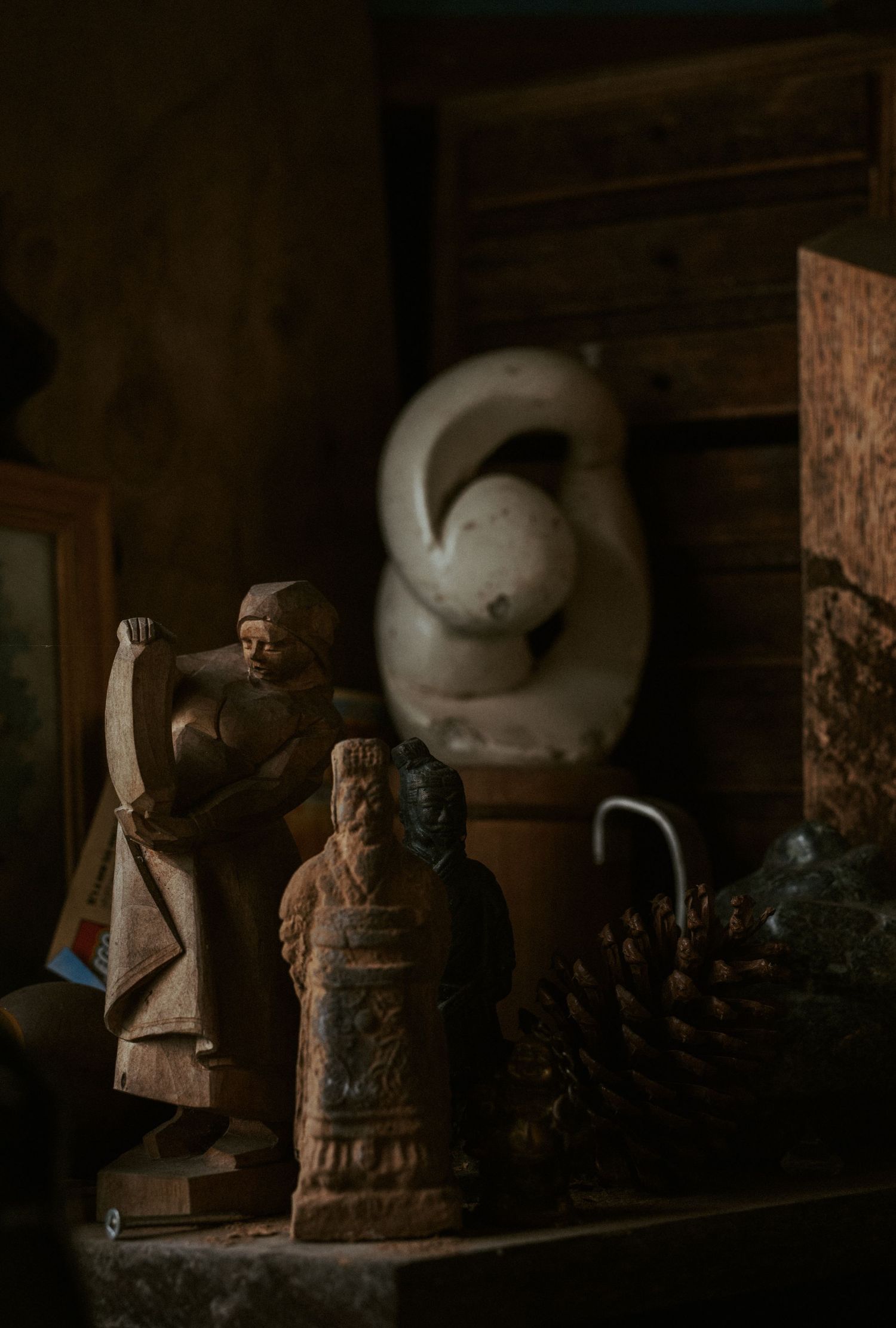 Dimly lit wooden shelves display a collection of carved sculptures and art pieces in a rustic studio setting.