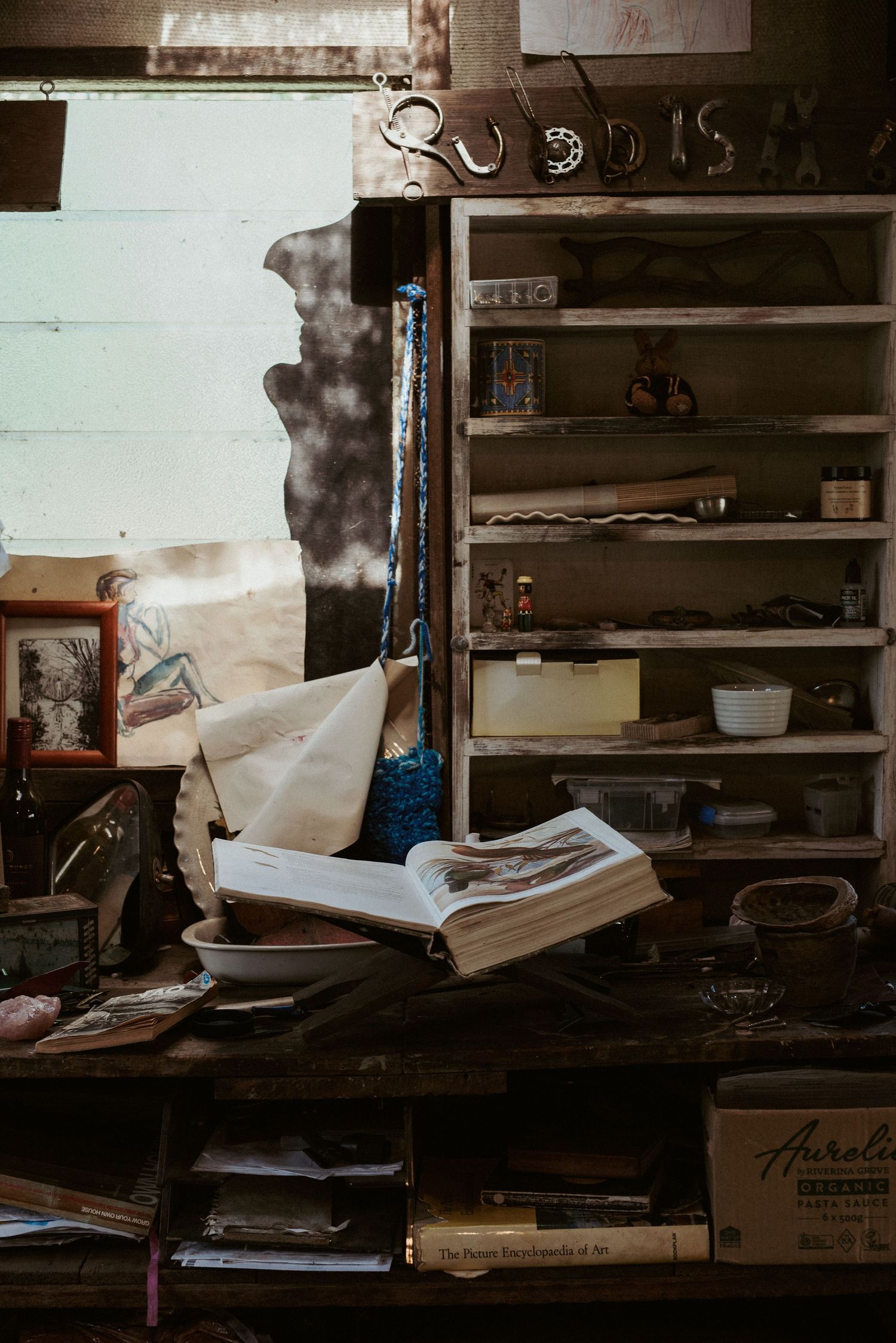 Cluttered workshop shelves filled with tools, papers and supplies in moody lighting.