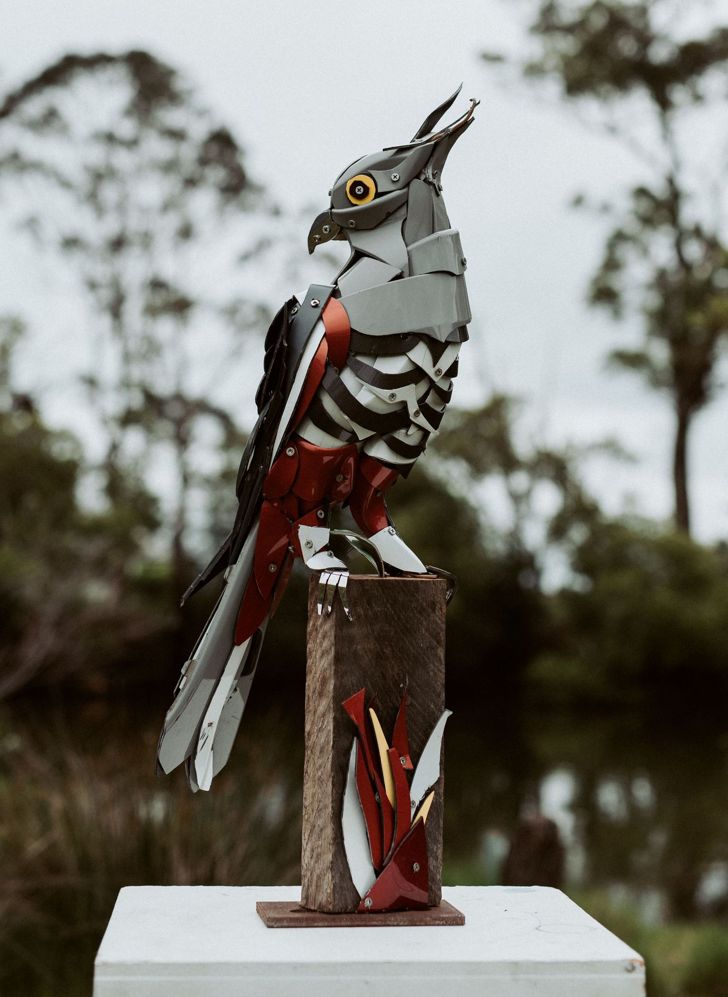 Geometric metal bird sculpture displayed on white platform outdoors.