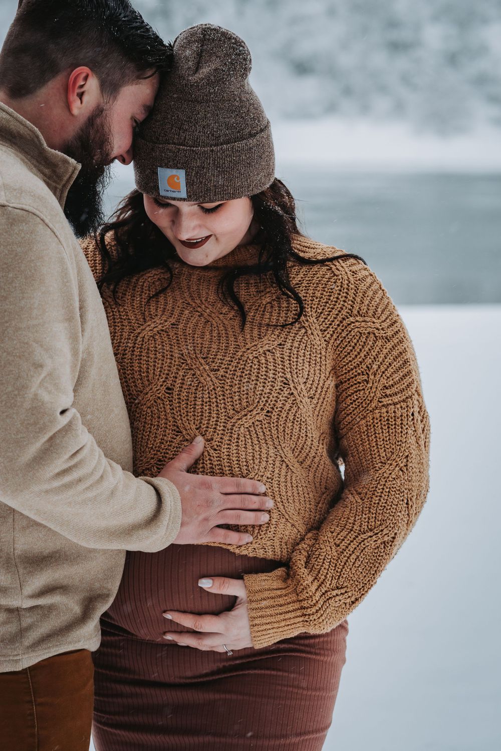 A serene winter maternity session by the lake, showcasing a glowing mother-to-be against a snowy backdrop in Post Falls.