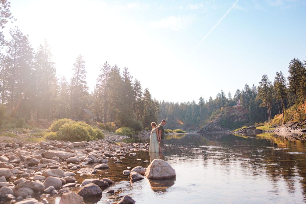 A pregnant couple stands gracefully in the river, captured during a Post Falls maternity session.