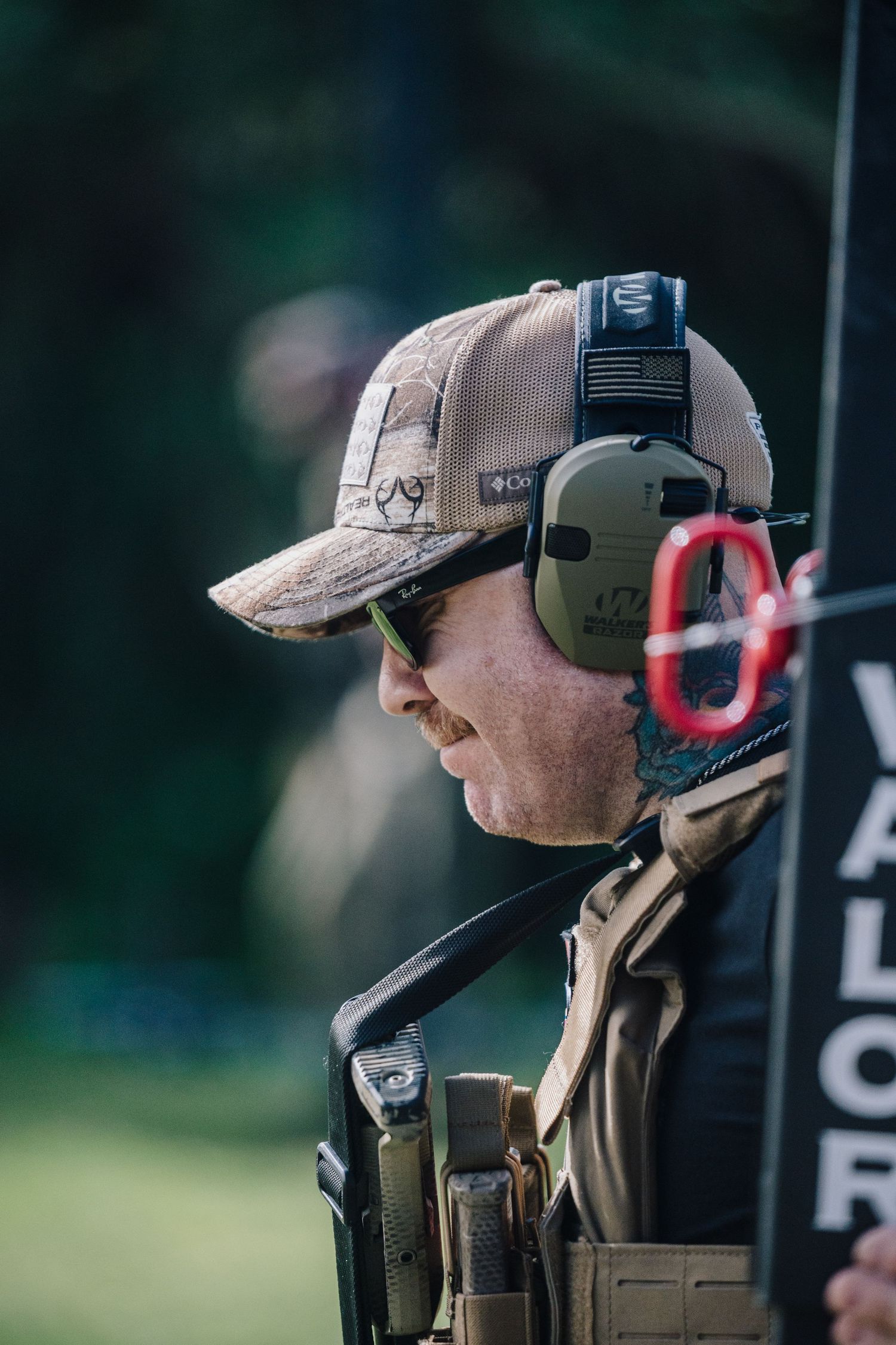 Side profile of shooter wearing ear protection and tactical gear at outdoor range.