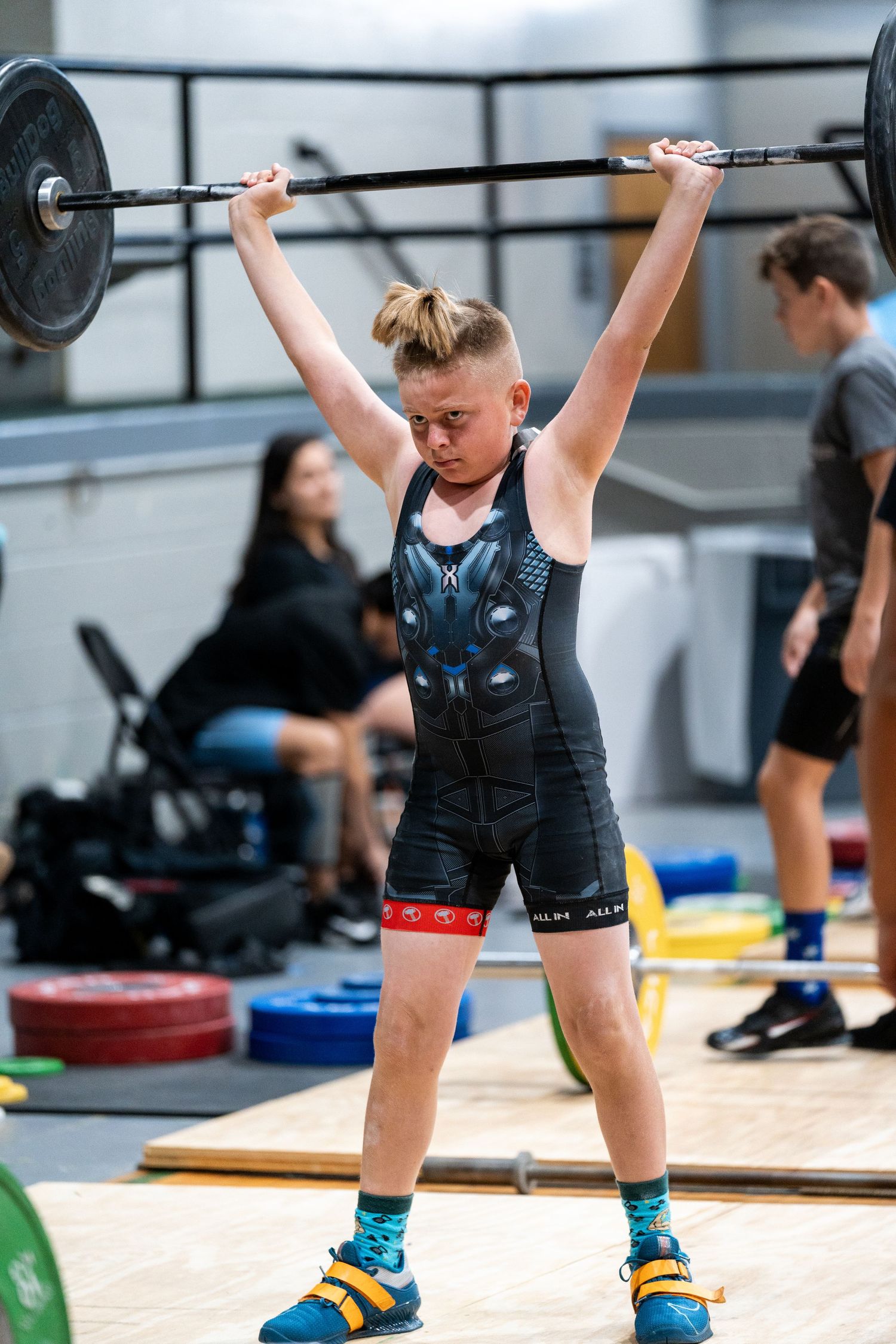 Young weightlifter holds barbell overhead during competition lift on wooden platform.