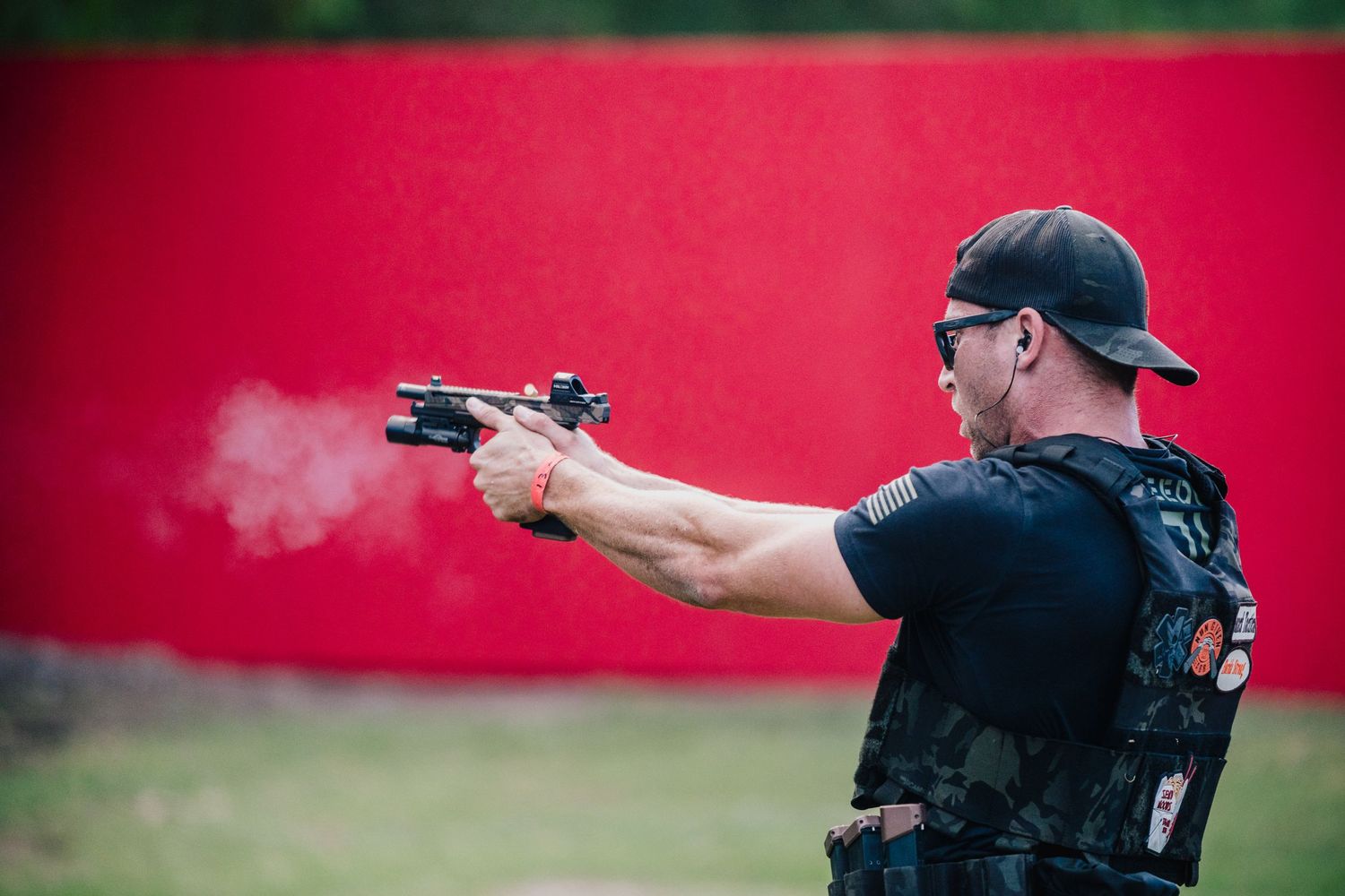 Shooter fires handgun with visible smoke trail against red background.