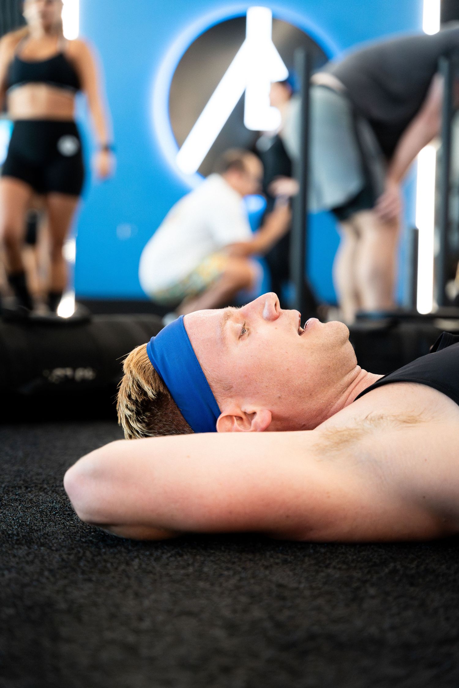 Exhausted athlete lying on gym floor wearing blue headband after intense workout.