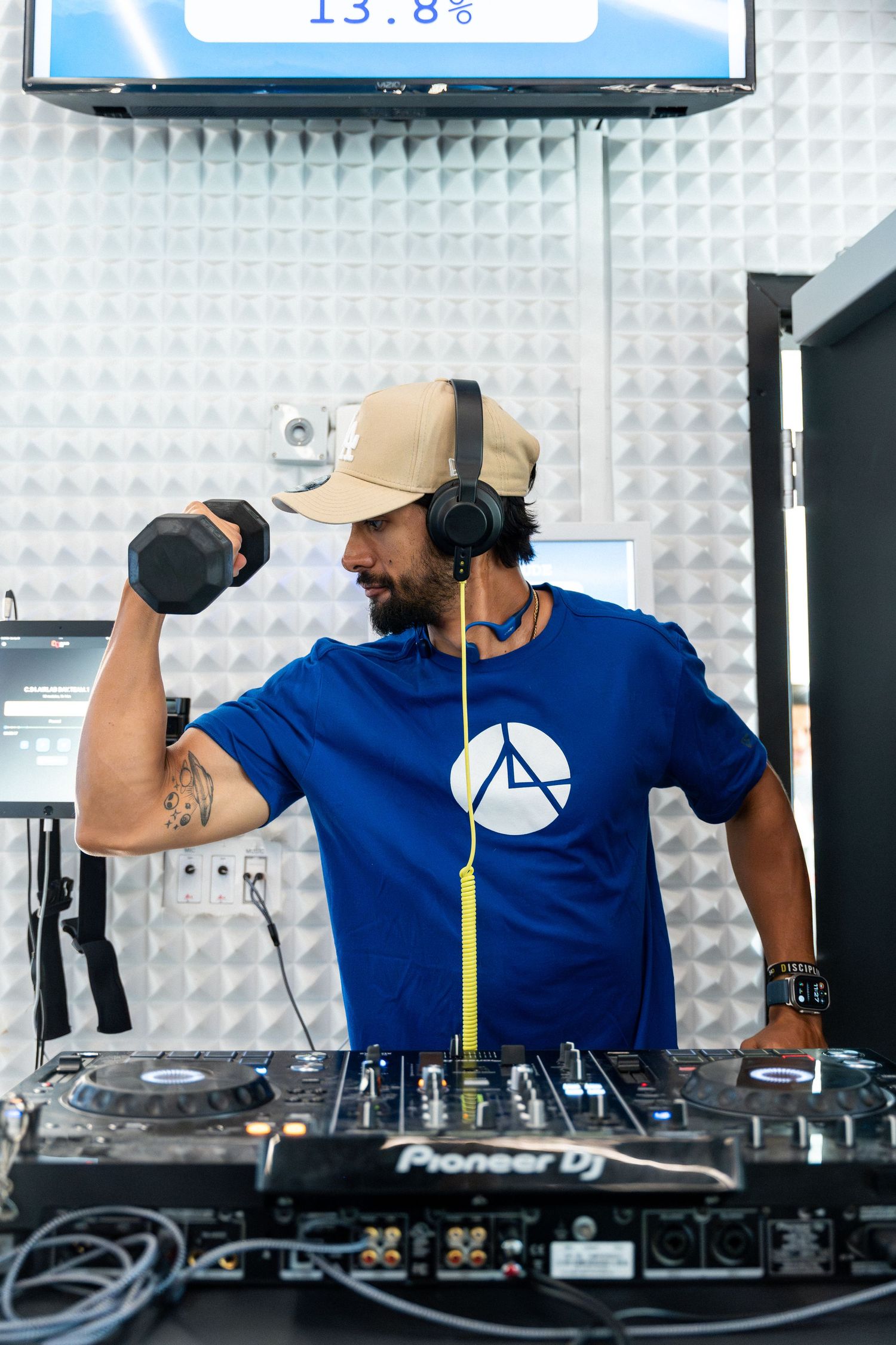DJ wearing blue t-shirt and baseball cap performing at fitness event with Pioneer equipment.