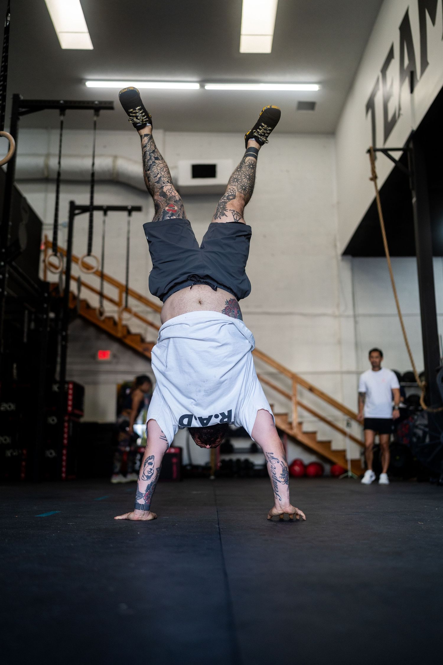 Tattooed athlete performing an inverted handstand during an intense workout session.