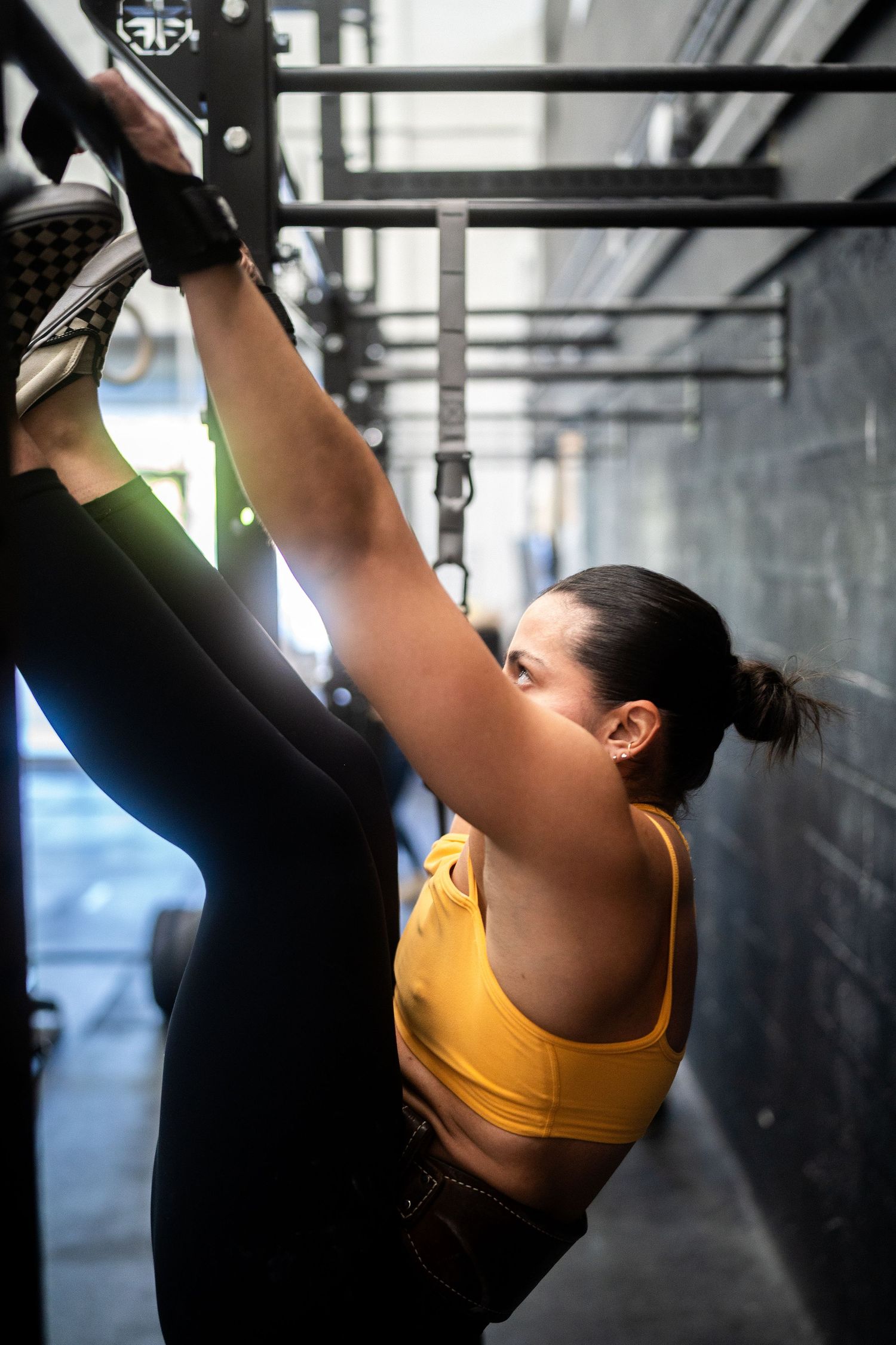 Athlete in yellow sports bra and leggings performing a high leg stretch on gym equipment.