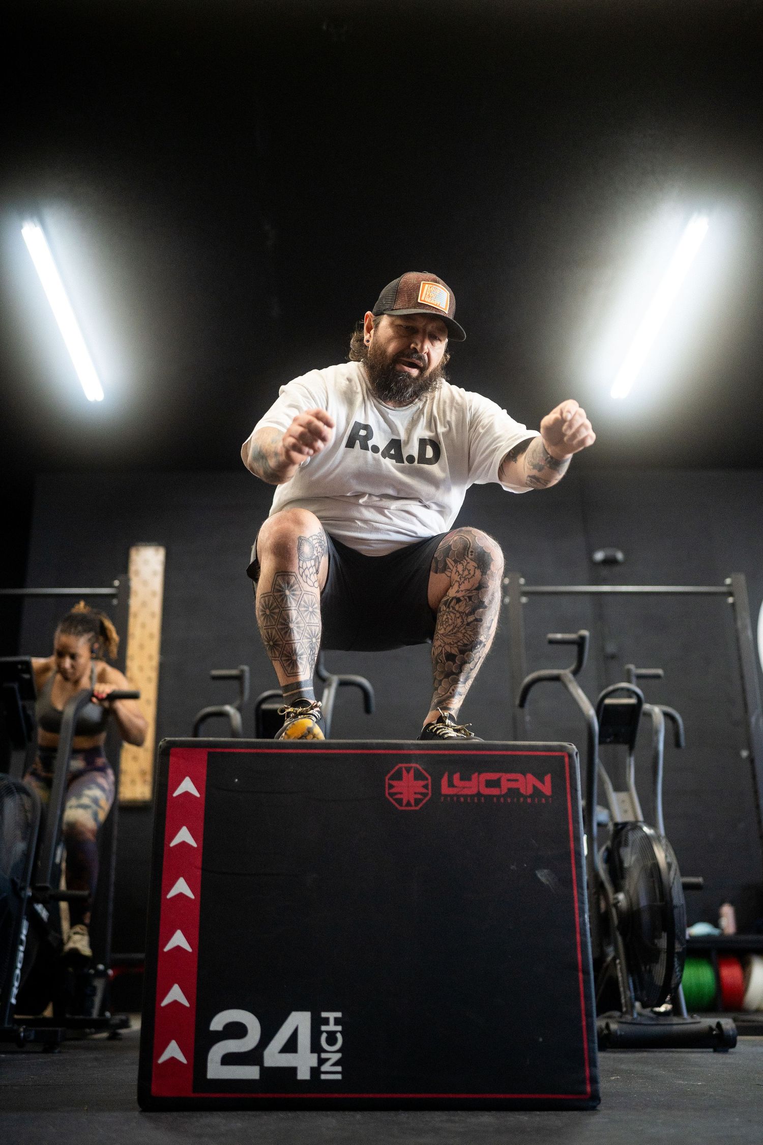 Athlete jumping onto a 24-inch box at a CrossFit gym with dramatic lighting.