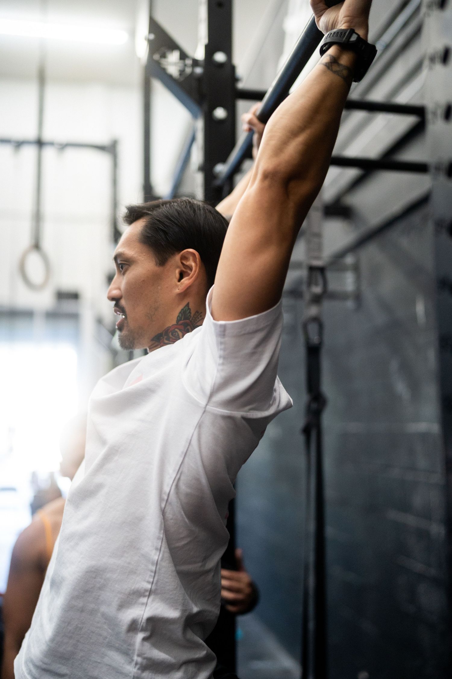 Athlete performing an overhead mobility exercise in a white shirt at a fitness facility.