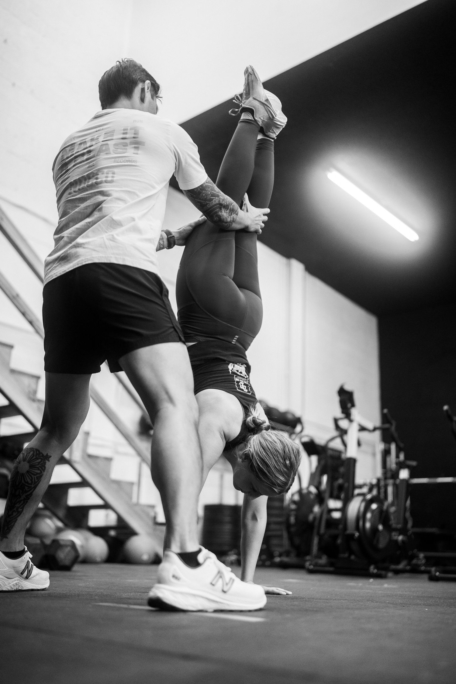 Athletes practicing handstand techniques with spotting assistance in black and white.