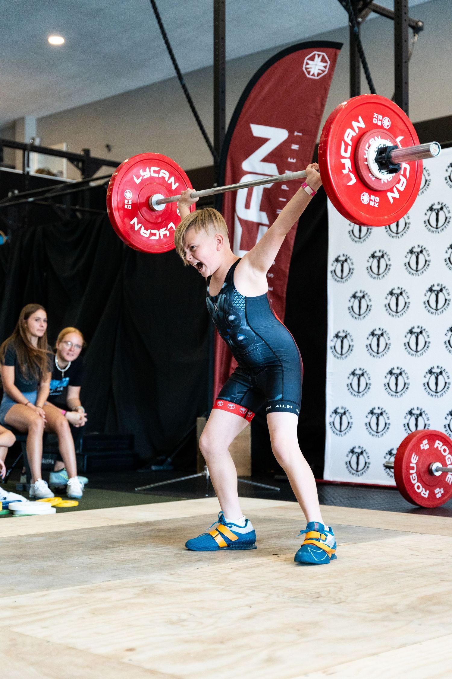 Olympic weightlifter performing a snatch lift with red competition plates during an event.