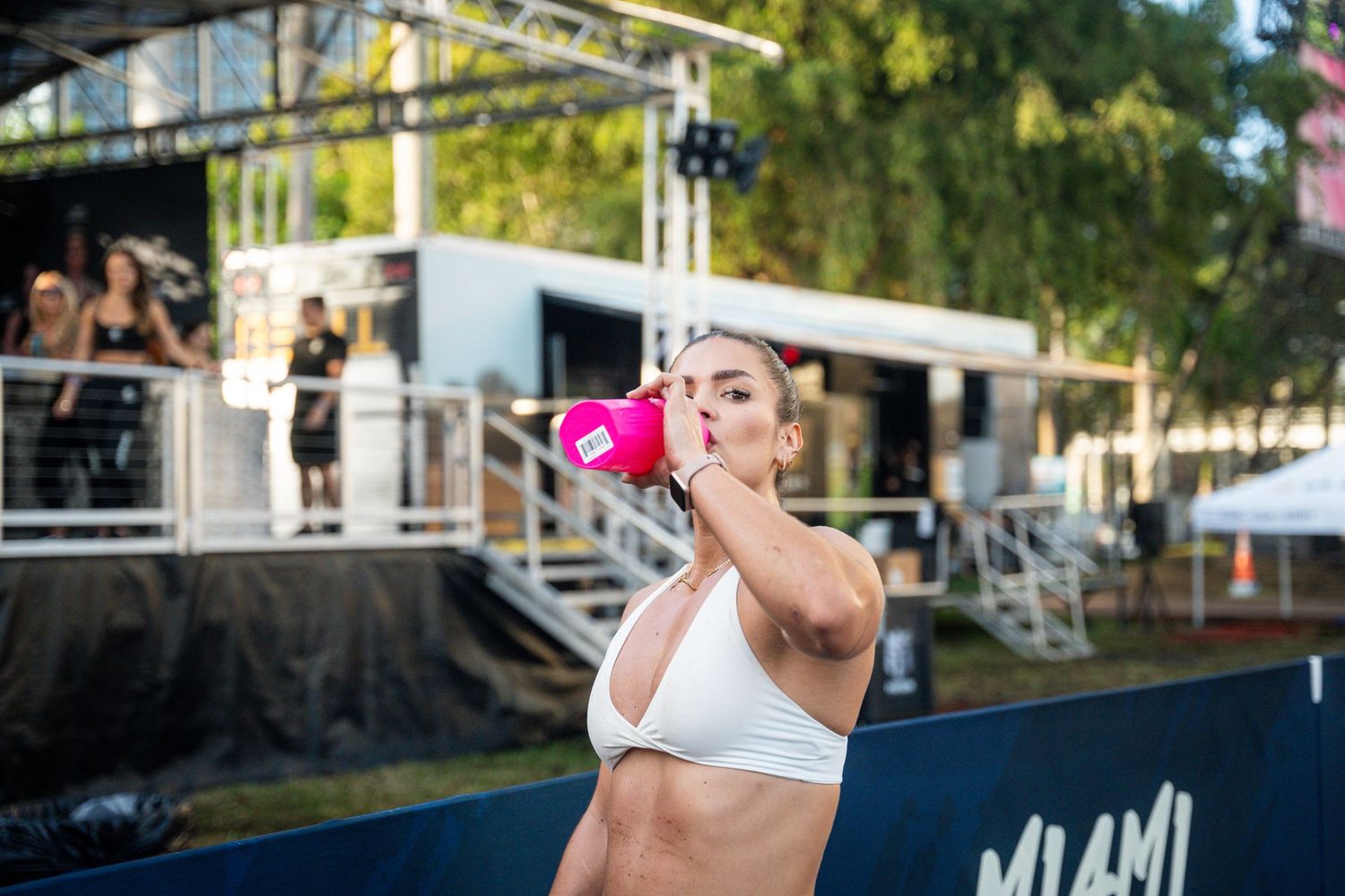 Athlete drinking from water bottle during outdoor fitness competition in Miami.
