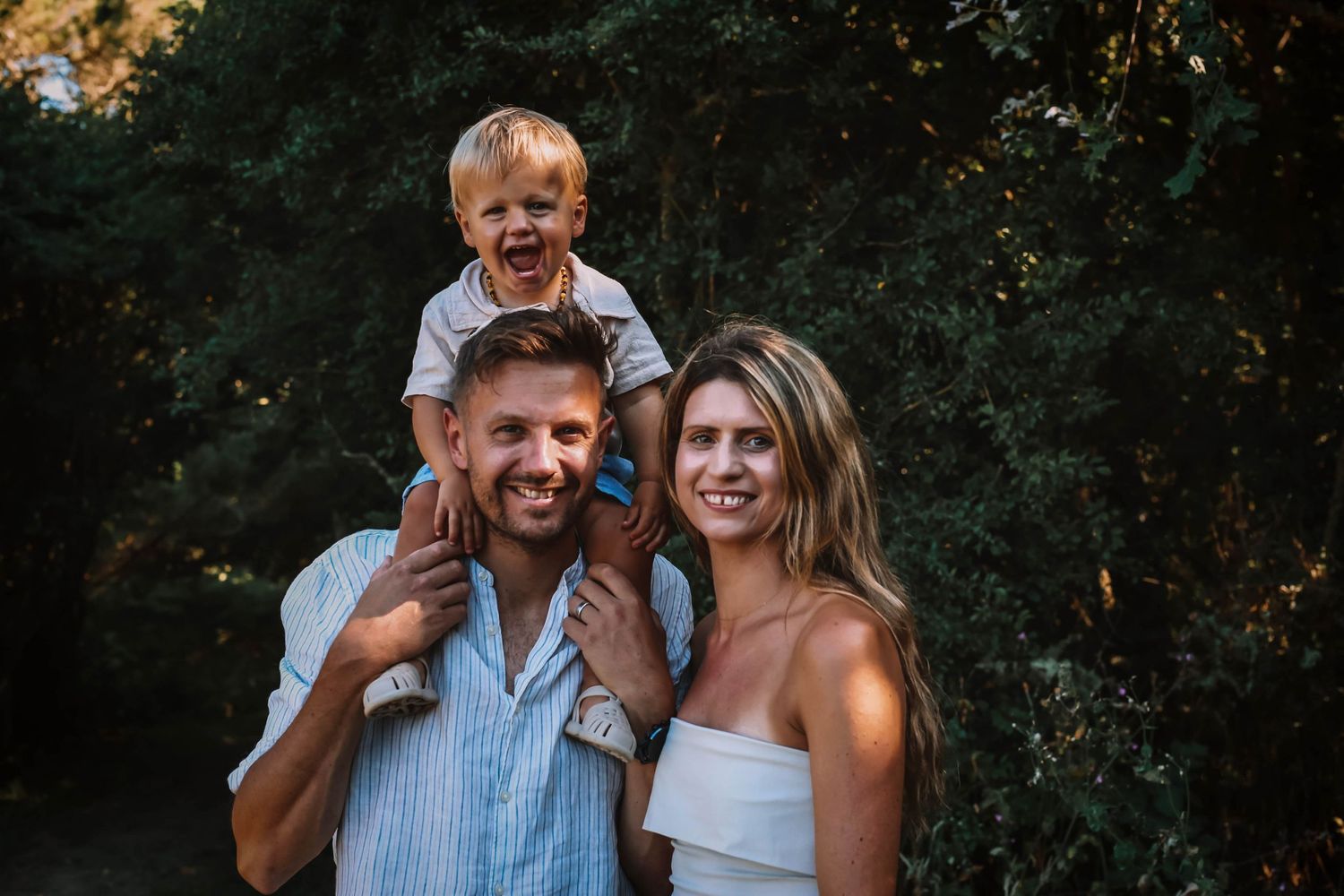 A family photography session in a wooded area with warm evening light.