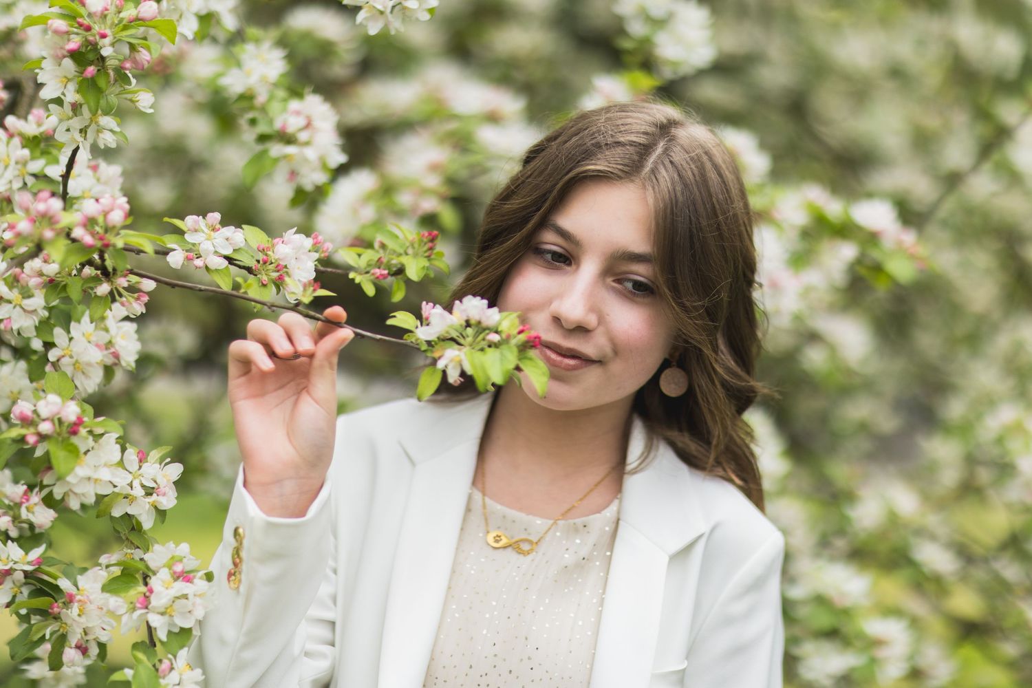 Woman in white blazer gently touches cherry blossoms in spring garden setting.