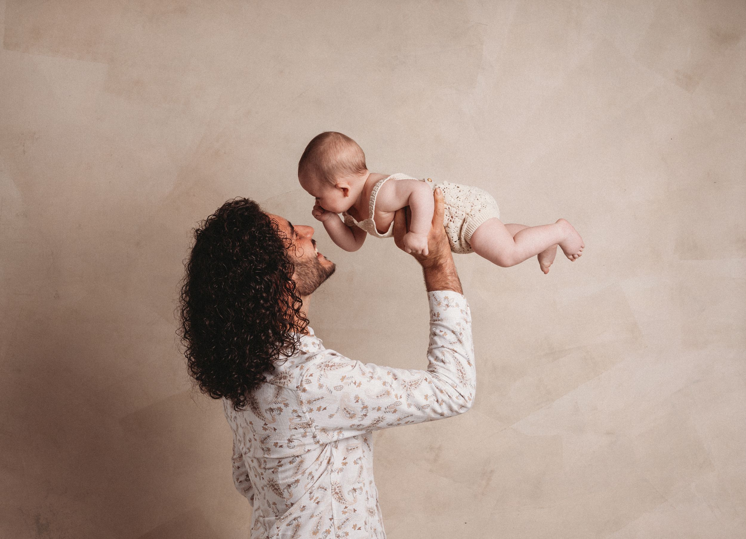 A series of seven artistic maternity photos showing a person in a white lace dress against a neutral beige backdrop.