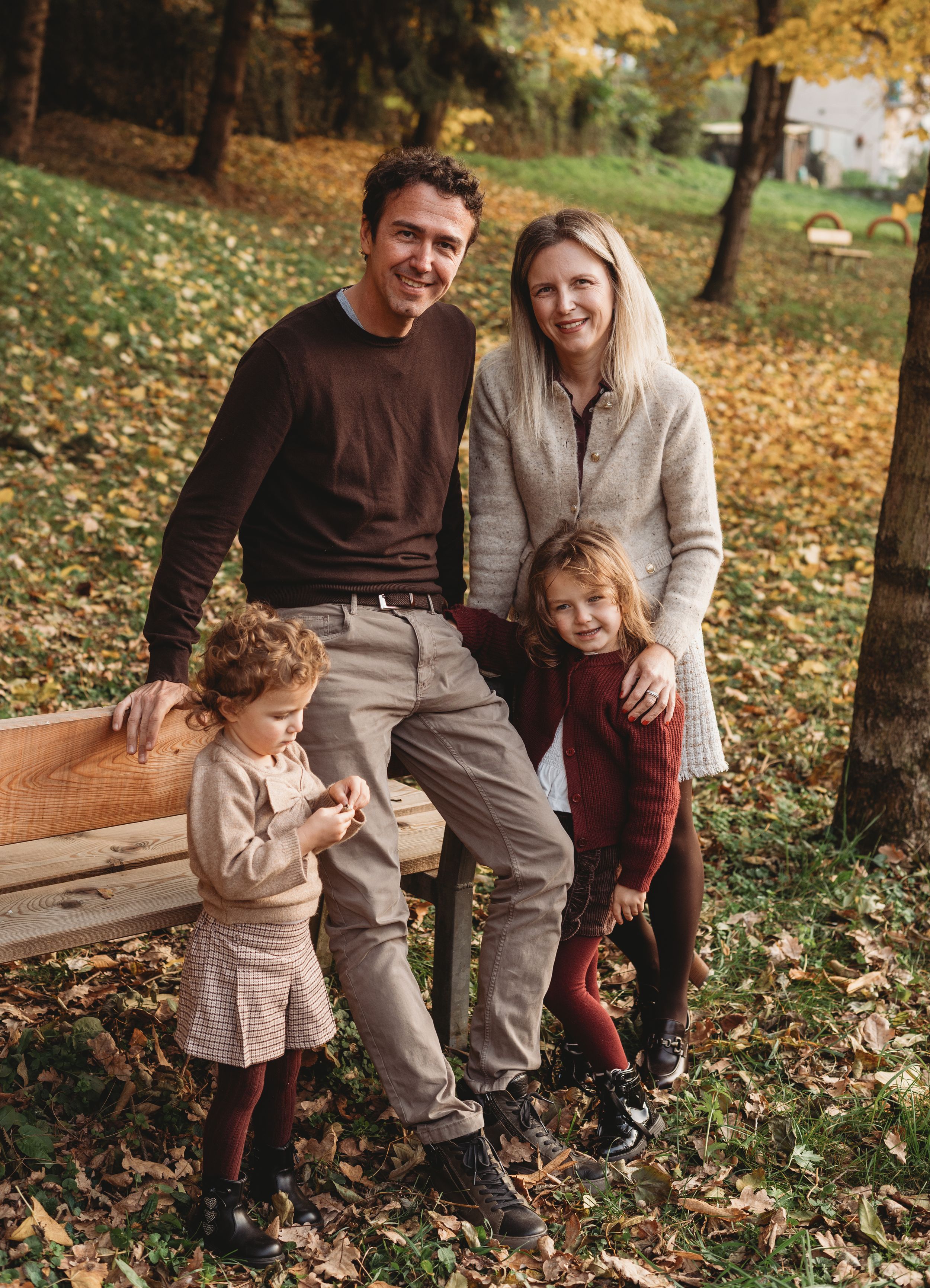 A family plays together in a park filled with fallen autumn leaves on a sunny afternoon.