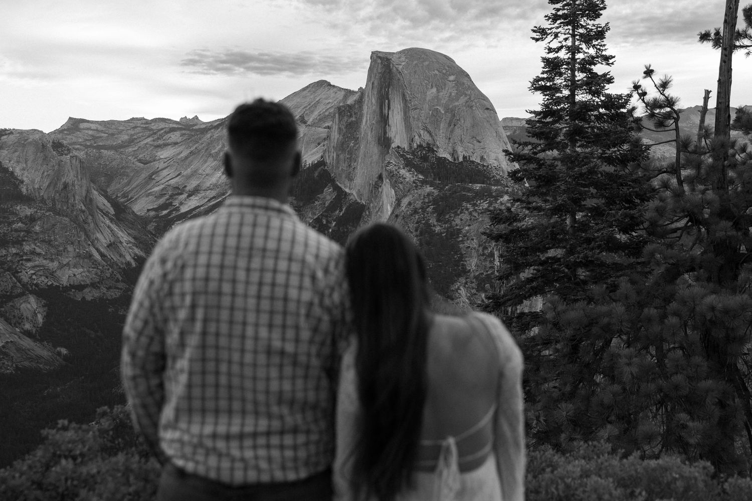 Black and white photo of couple admiring Half Dome view at Glacier Point Yosemite.