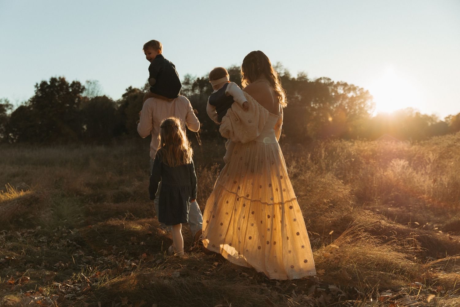 family of five walking away from the camera in a golden field during sunset