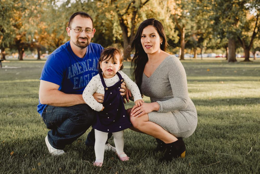 Family of three poses together on grass during sunset photo session.
