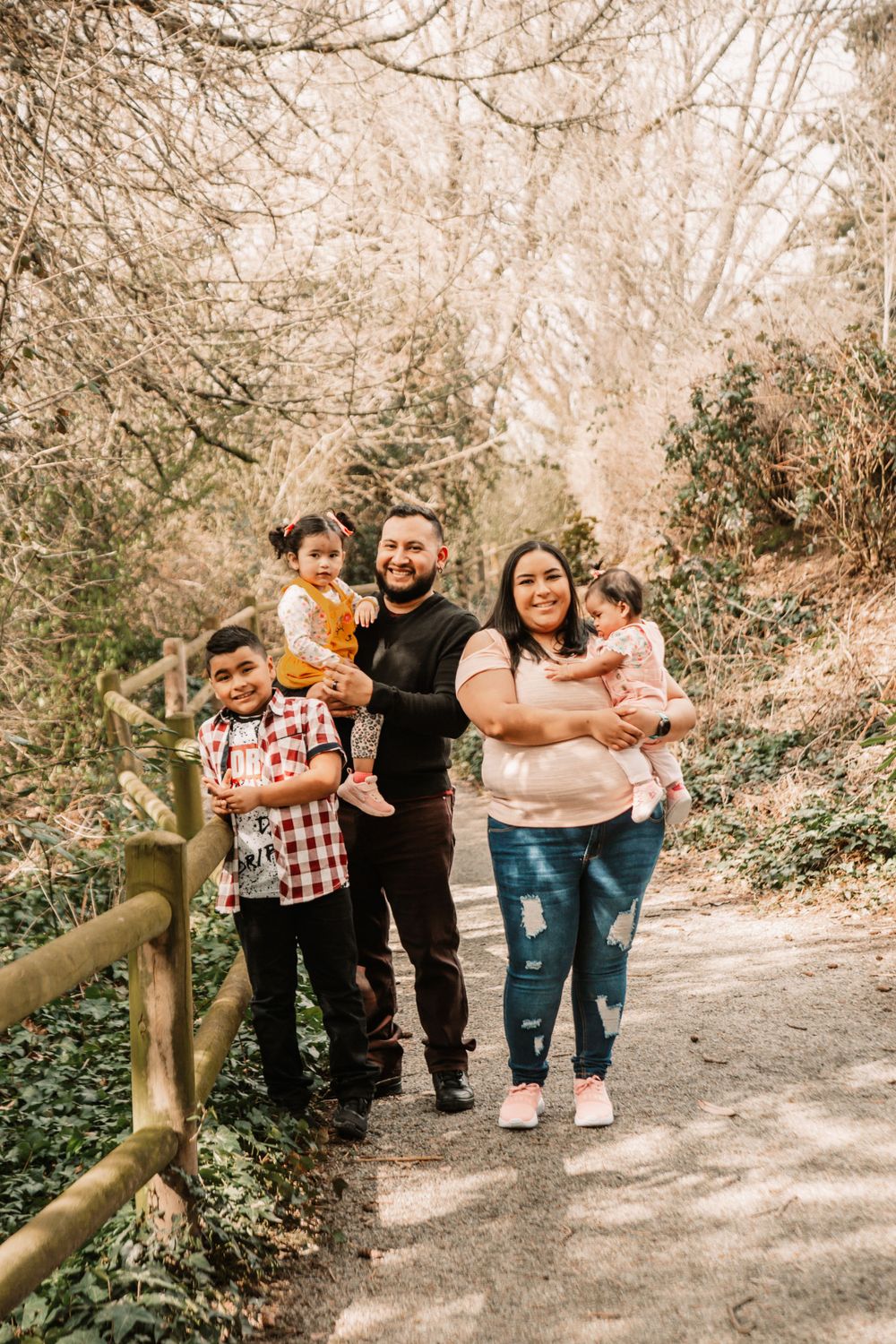 A family poses together on a nature trail with wooden railing and autumn trees.