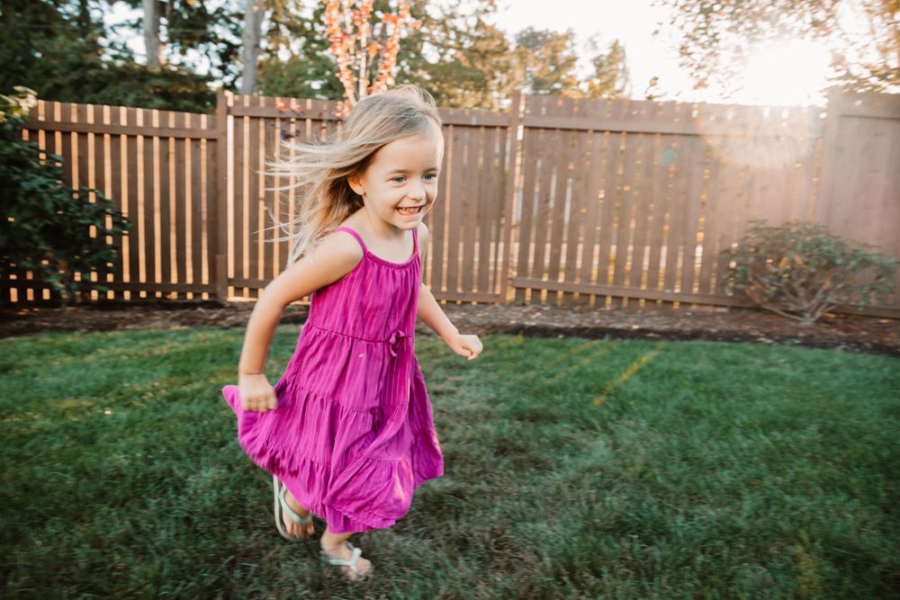 Child in flowing pink dress runs playfully in backyard during golden hour.