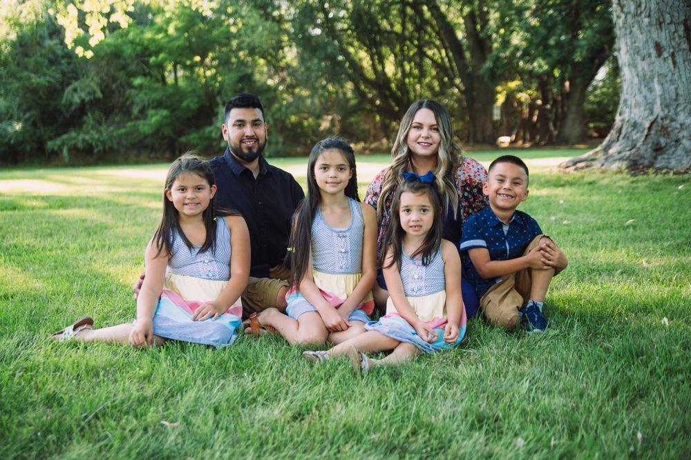 Family group sits together on lush green grass during summer evening photoshoot.