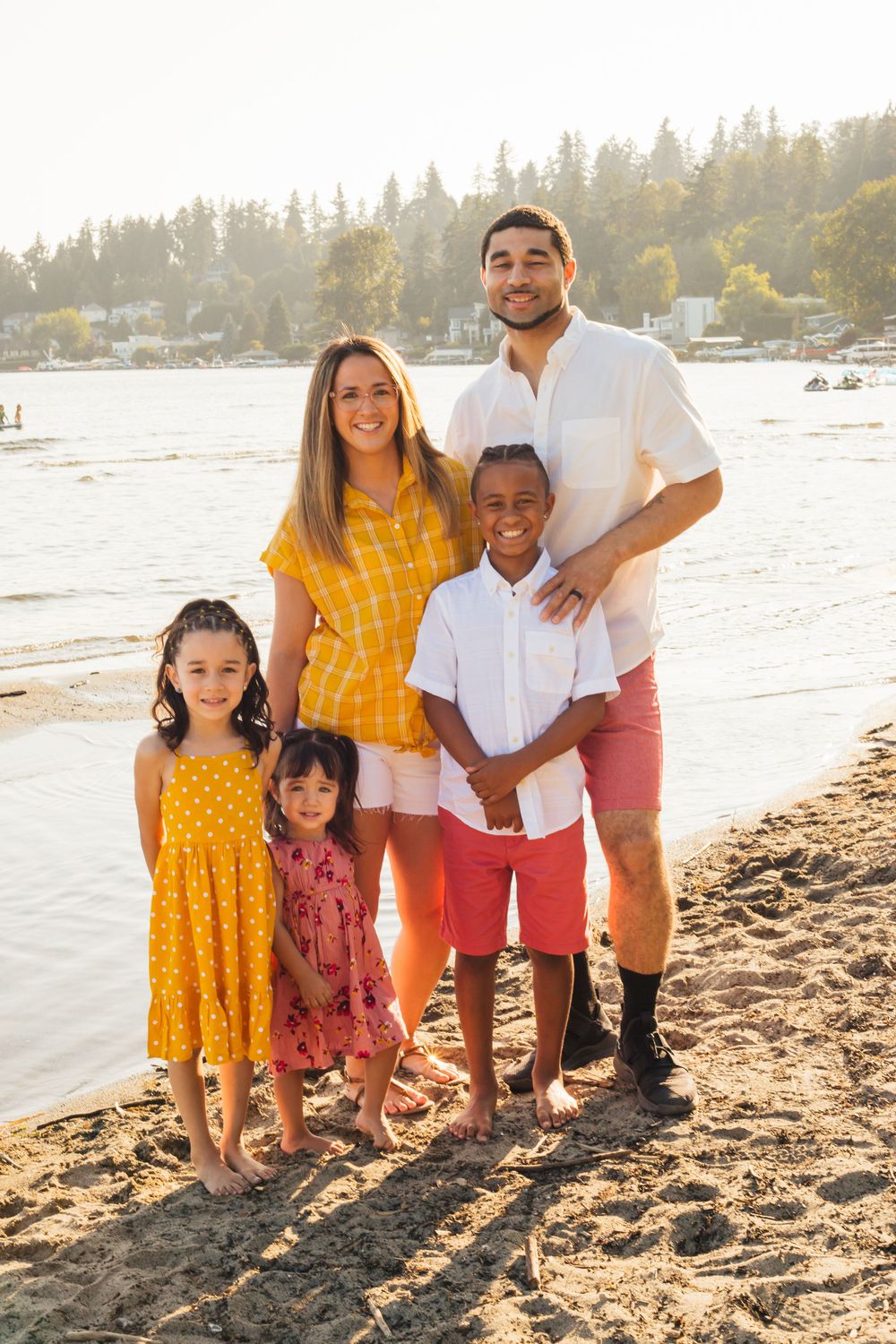 Family in coordinated yellow and red outfits posing together on a beach at sunset.