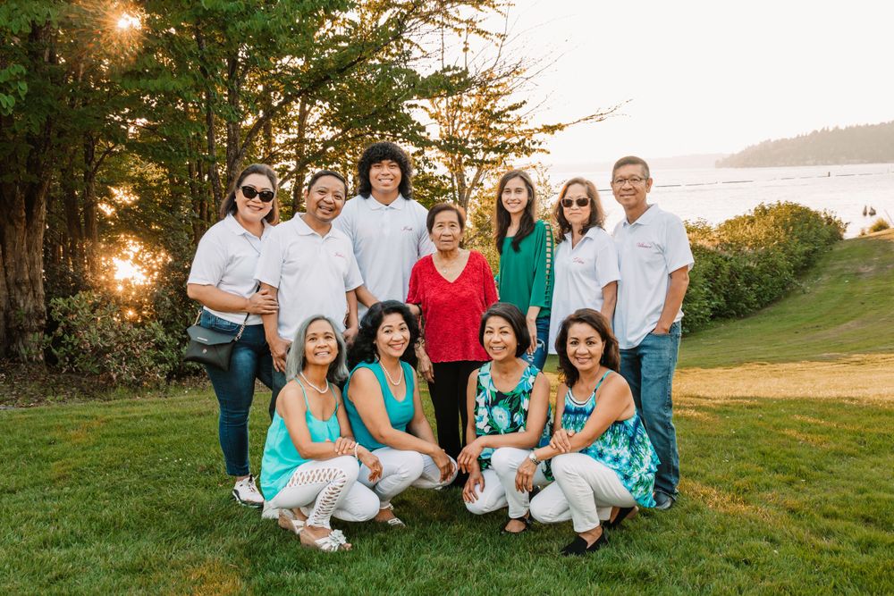A group portrait on a grassy hillside at sunset with people wearing coordinated white and turquoise outfits.