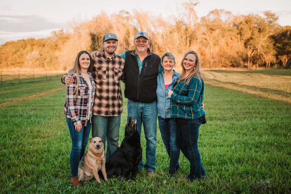 Family poses together in plaid shirts with their golden retriever in a grassy field at sunset.