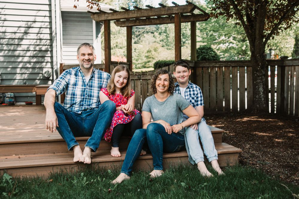 A family sits together on wooden deck steps in their backyard.