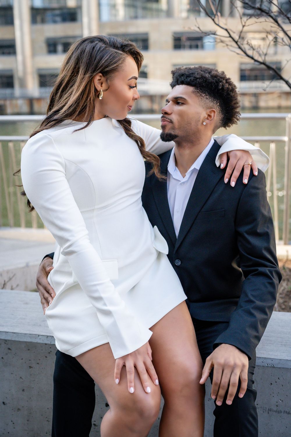 A couple in contrasting white and black outfits poses together on an urban terrace.