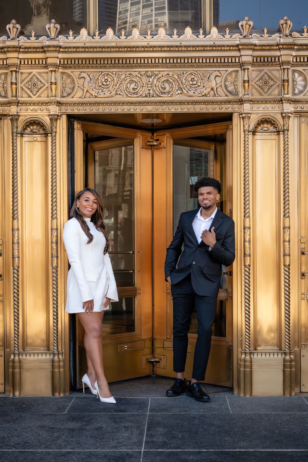 A couple poses in front of ornate golden doors in downtown Chicago.
