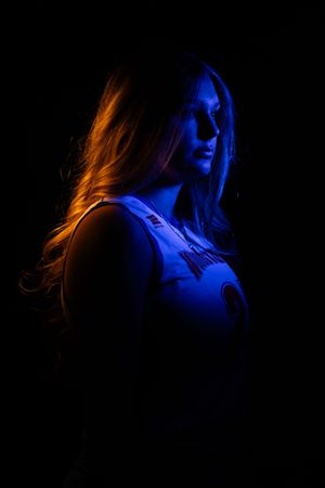 Woman illuminated by blue and orange lights against dark background, dramatic portrait photography. Salem County Senior Portraits
