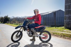 Senior Portrait of a boy riding a dirt bike in front of a rural barn on a sunny day.