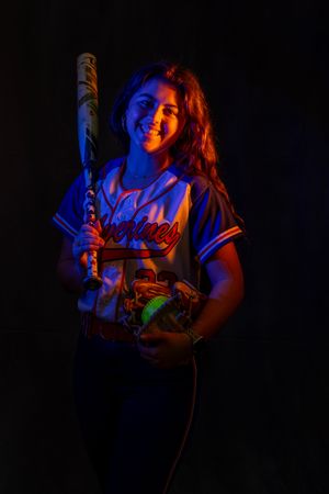 A senior Woodstown softball player poses with a bat under dramatic orange and blue lighting.