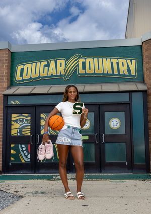 Female basketball player poses holding ball and letter in front of Cougar Country school entrance sign. SJ Senior Portaits