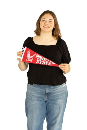 Smiling young woman holding a red Montclair State University pennant, wearing a black top and jeans on white background. Senior Portaits