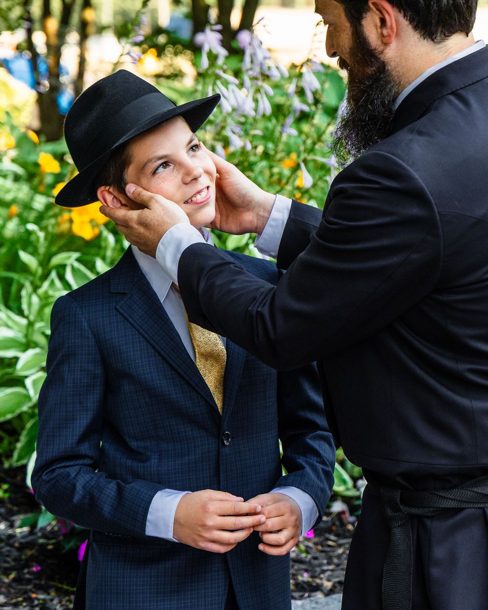 Two people share a playful moment outdoors with one adjusting the other's black fedora hat.