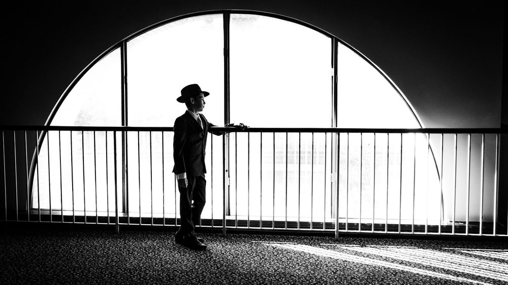 A dramatic black and white silhouette of a person standing by a window with strong light casting shadows.