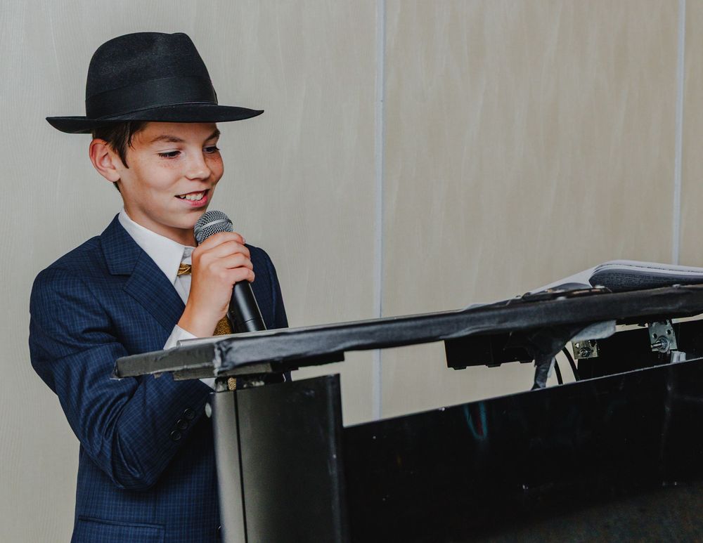A person in a navy suit plays a grand piano in a dimly lit room.