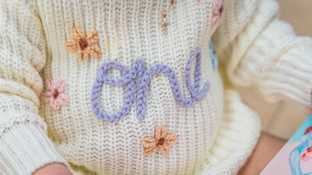 Close-up view of delicate embroidered flowers on white knitted fabric with pink and purple floral designs.