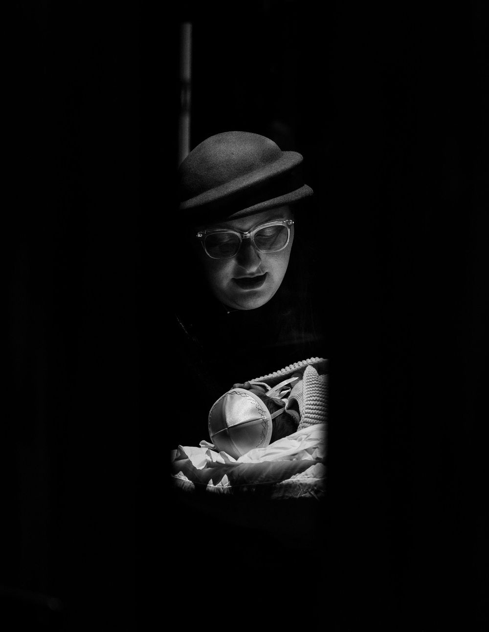 A dramatic noir-style black and white portrait showing a figure in shadow wearing a fedora hat and glasses.