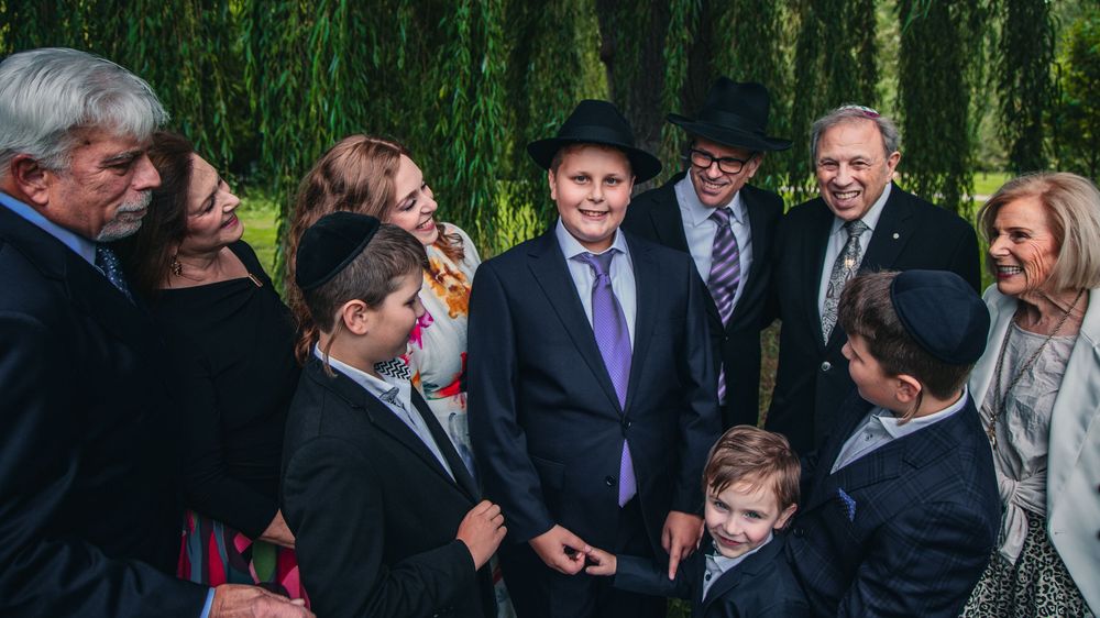 A group of formally dressed people gathered outdoors with weeping willow trees in the background.