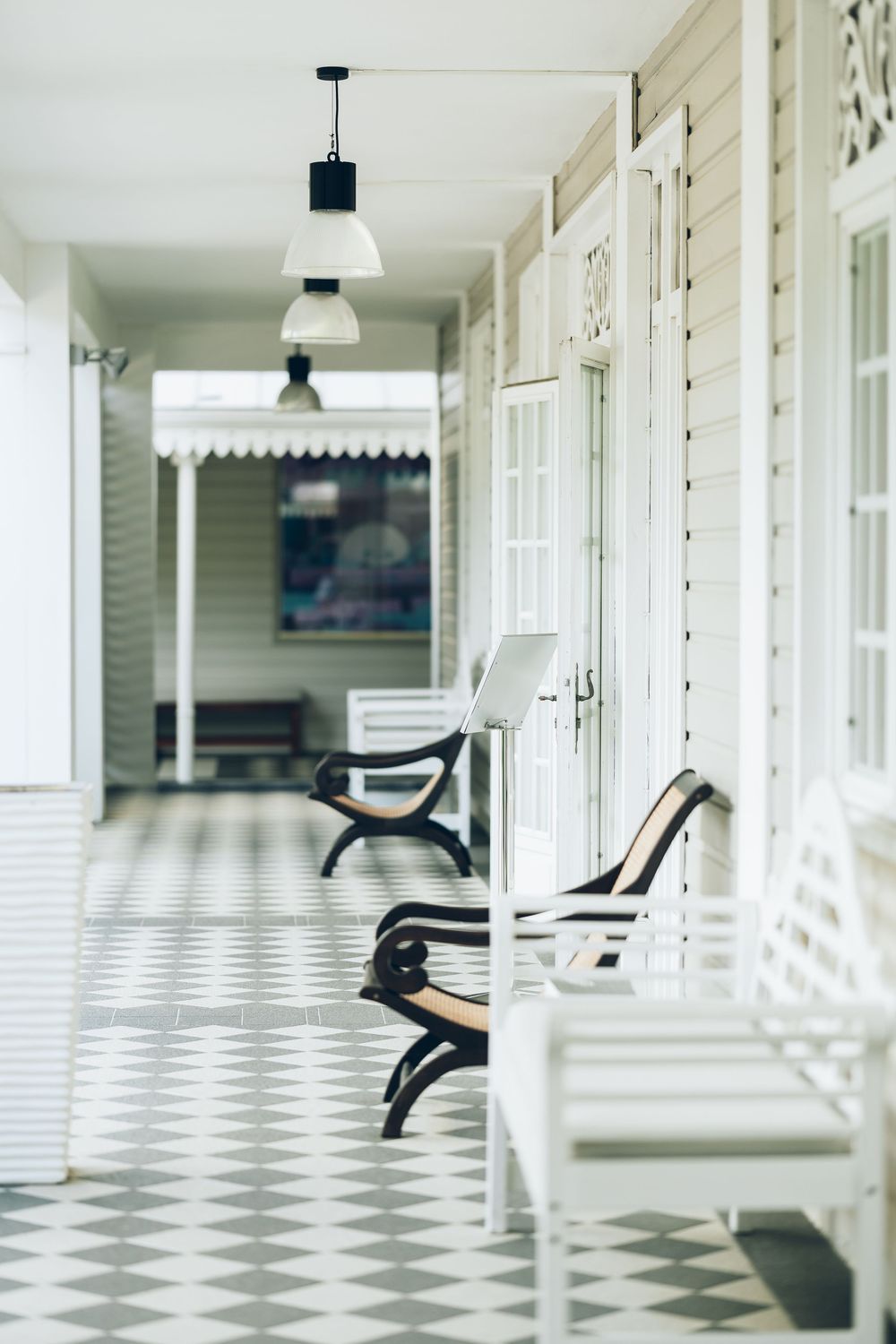White wooden chairs line a checkered tile porch with pendant lights and elegant colonial architecture.