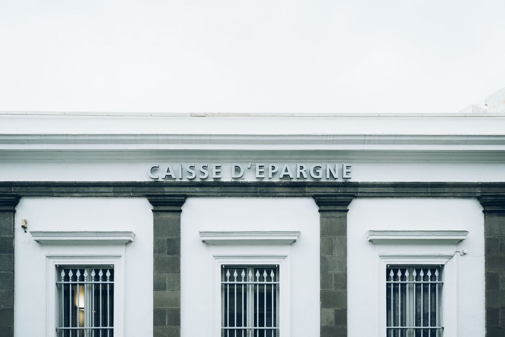 Caisse d'Epargne bank branch facade with white classical architecture, barred windows, and bold signage.