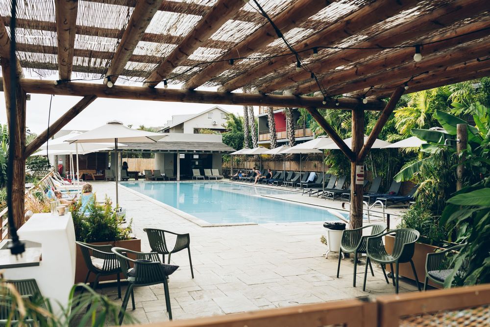Covered outdoor poolside seating area with tables and chairs under a rustic wooden pergola structure.