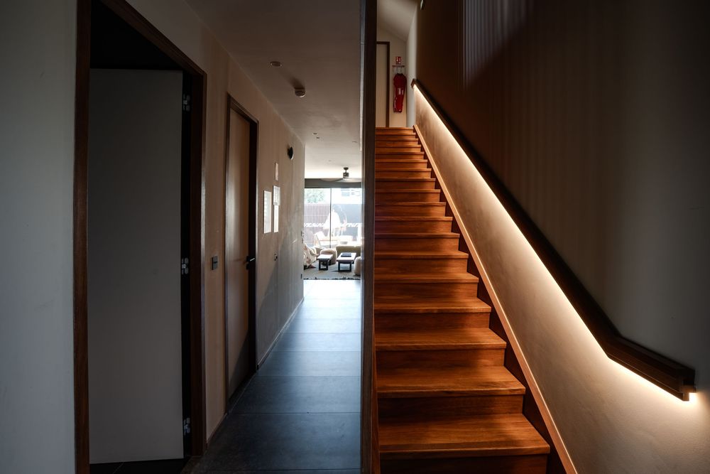 Modern hallway with wooden staircase featuring LED strip lighting, dark tile floors, and doors leading to bright rooms.