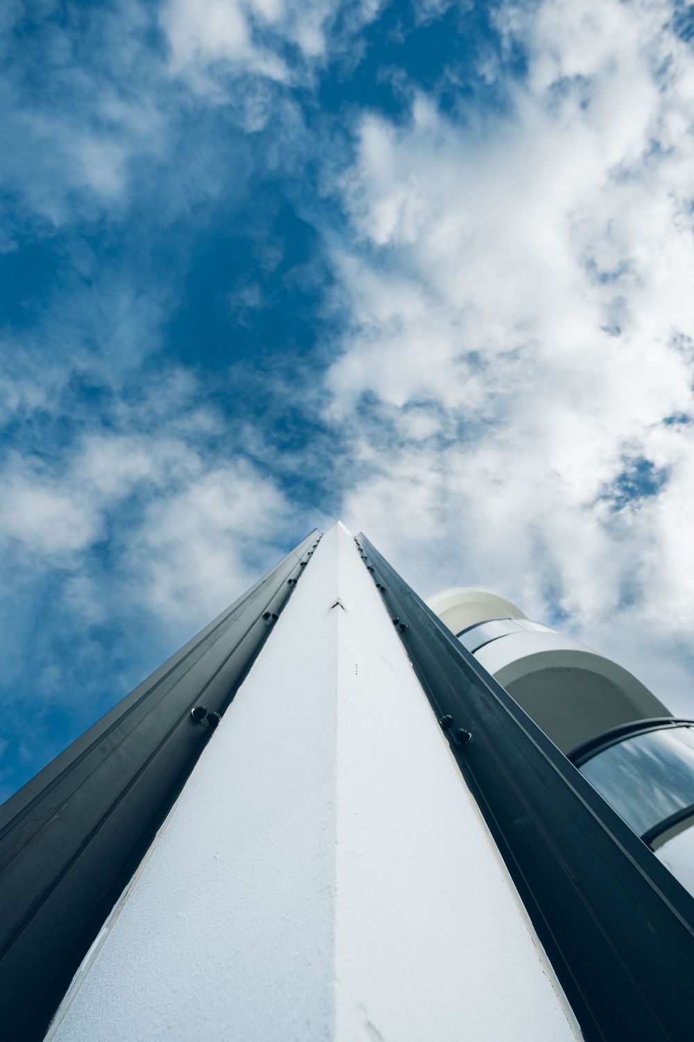 Low angle view of a white lighthouse tower against a blue sky with scattered clouds.